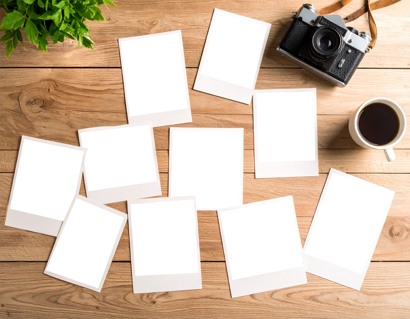 木製デスクに散らばるインスタント写真フレームとレトロカメラ、コーヒーの俯瞰。温かみのある木製デスクに、空白のインスタント写真フレームが複数散らばり、アンティークカメラと温かいコーヒーが置かれた真俯瞰の風景です。