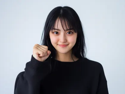 笑顔で拳を握る日本人女性のポートレート。黒いセーターを着た若い日本人女性が、優しい笑顔で力強く拳を握りしめているポートレート写真です。