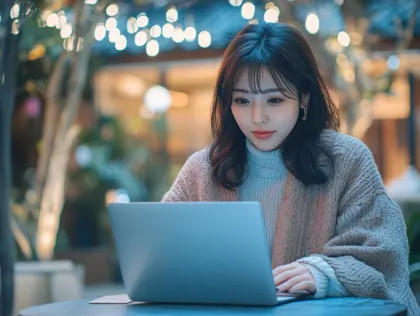 夜カフェでノートPC作業に集中する日本人女性。イルミネーションが輝く夜の屋外カフェで、カジュアルな服装の日本人女性がノートパソコンに集中しています。